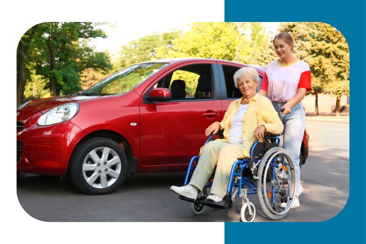 Person standing next to senior adult in a wheelchair, a car is in the background