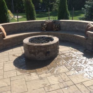 Backyard of home with stamped concrete patio, a concrete fire pit, and concrete wall with bench seating