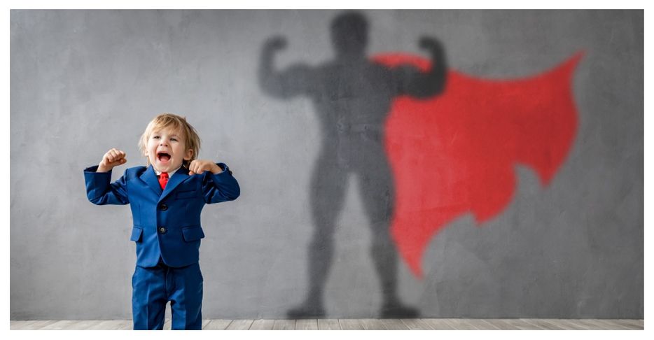 Boy in suit flexing, superhero shadow behind him.