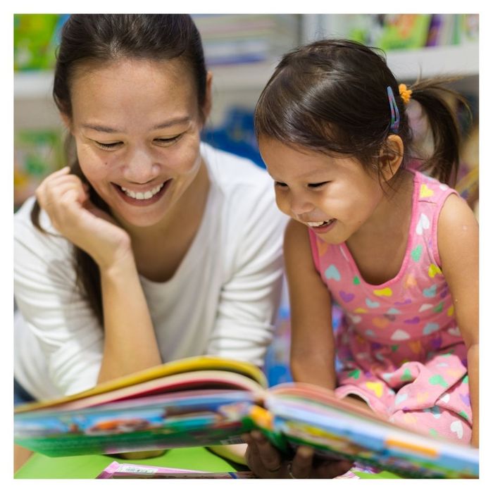 Mother and daughter happily reading colorful book together.