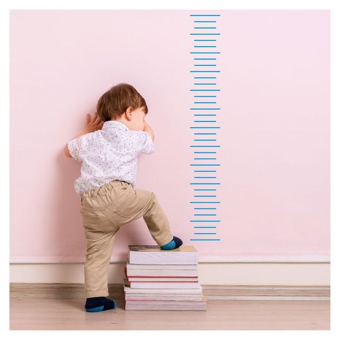 Toddler stepping on books, measuring growth on wall.