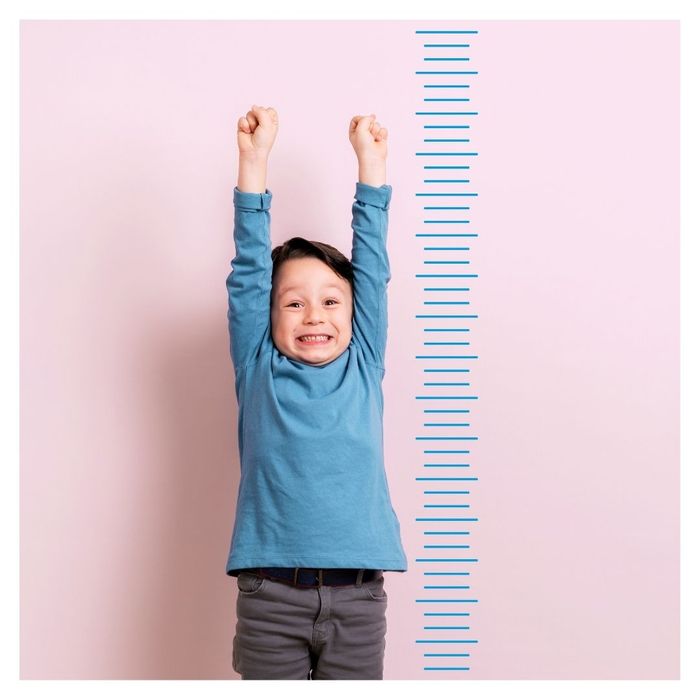 Smiling child stretching arms next to growth chart.