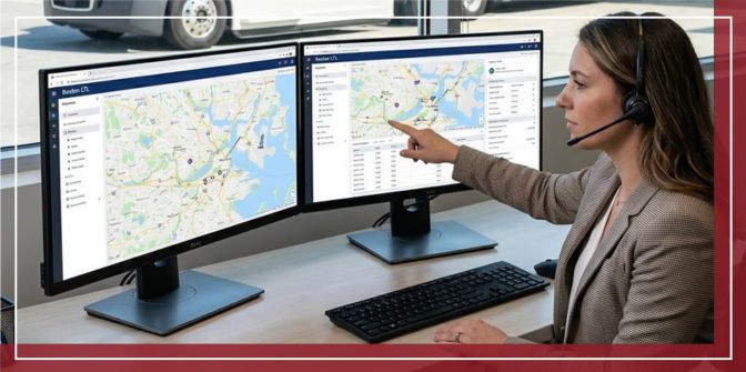 A customer service representative in a Boston logistics center, seated at a desk with modern tracking software on dual monitors, points to a map showing an LTL shipment.