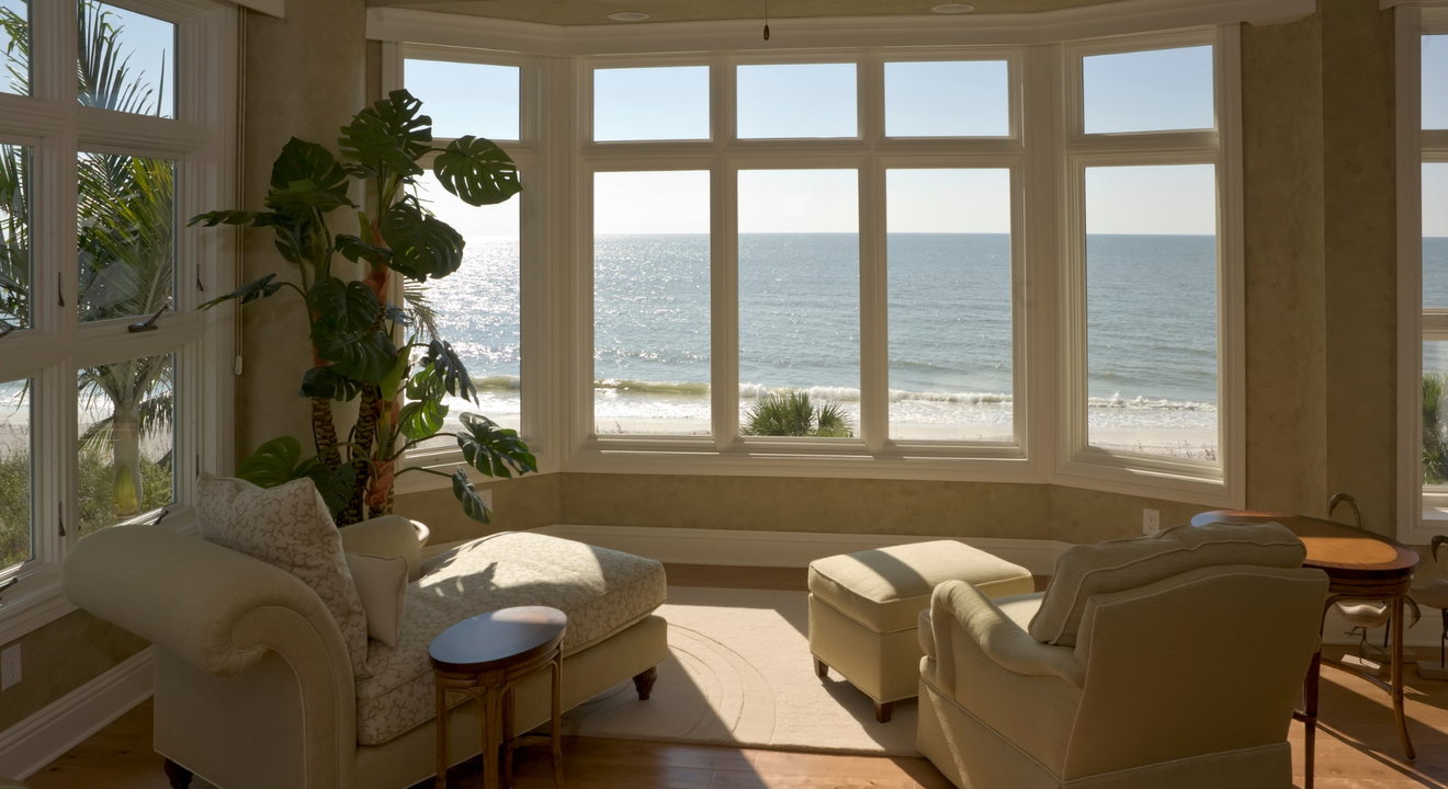 Modern coastal home exterior with large clear windows under a cloudy sky Modern coastal home exterior with large clear windows under a cloudy sky