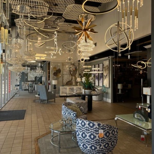 A wide view of a spacious lighting store with high ceilings, displaying numerous contemporary ring-shaped pendant lights, geometric fixtures, and crystal chandeliers over a tiled floor.