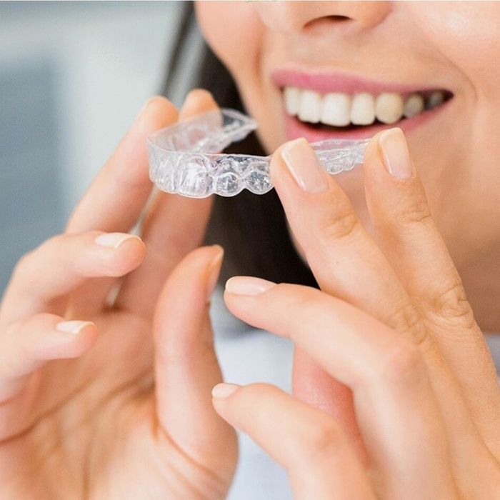 Close up of woman holding clear aligners near her mouth