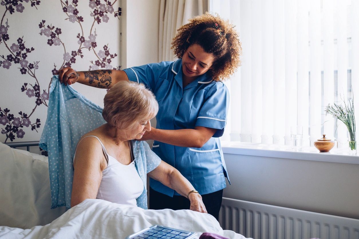 nurse putting an elderly woman's shirt on while the elderly woman sits down