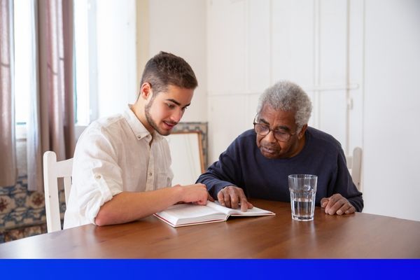 young man reading a book to an older man