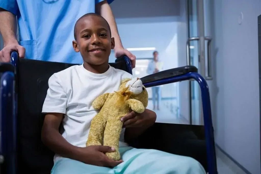 a boy sitting on a wheelchair and holding a teddy bear