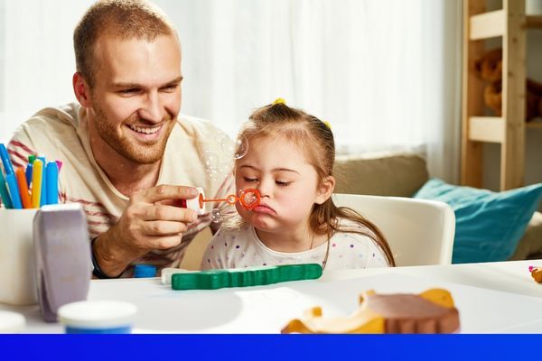a man blowing bubbles with a little girl with down syndrome