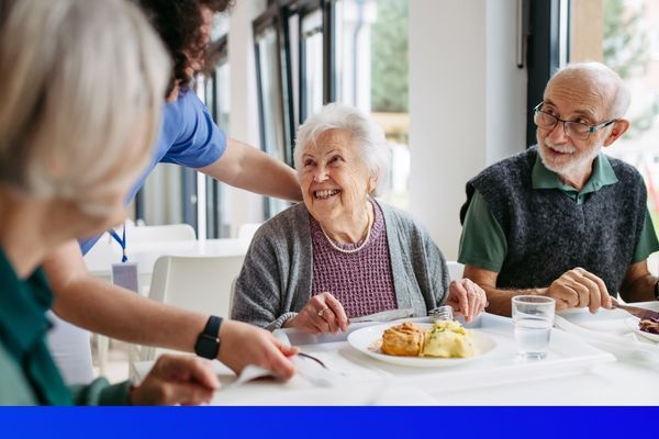 old man and old woman smiling at nurse as they get food