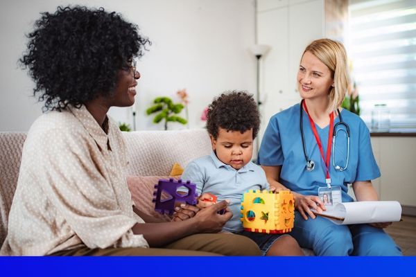 a nurse, mother, and little boy sitting on the couch while the little boy plays with toys