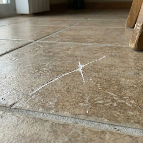 A close-up view of deep, visible white scratches on a textured brown stone floor tile, likely caused by dragging furniture.