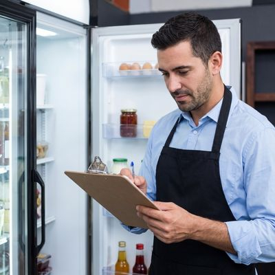 Business owner reviewing paperwork on a clipboard near a refrigerator.