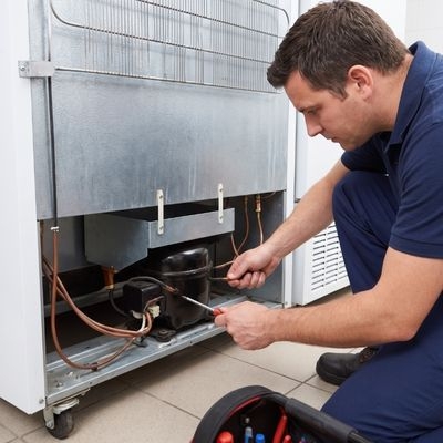 Technician diagnosing mechanical components behind a commercial freezer.