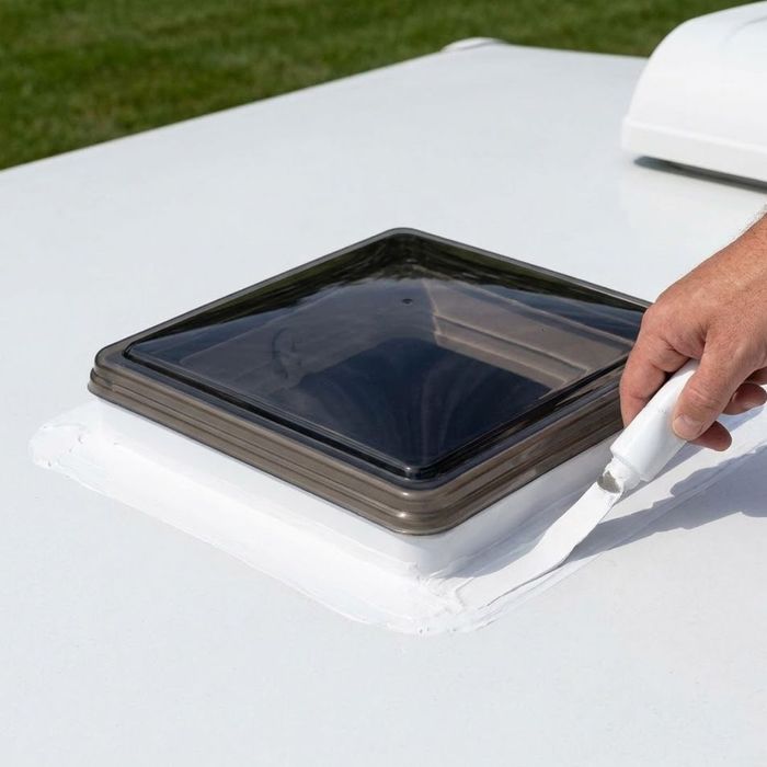 Hand applying white lap sealant around an RV roof vent.