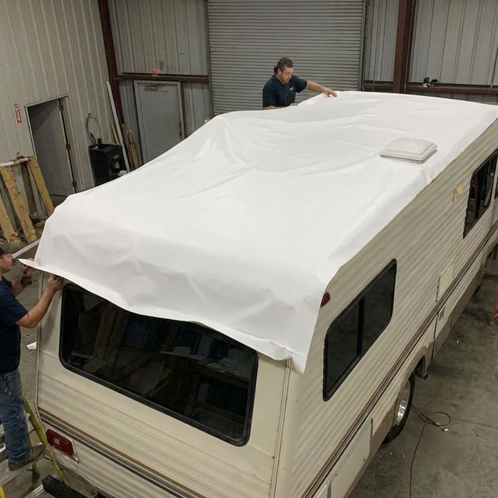 Workers installing a large sheet of white membrane on a refurbished RV roof.