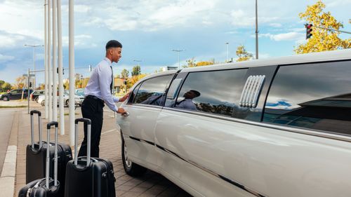 Man opening the door of a limo for his passengers. 
