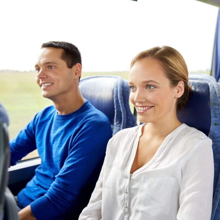 Man and a woman sitting next to each other on a charter bus, smiling. 