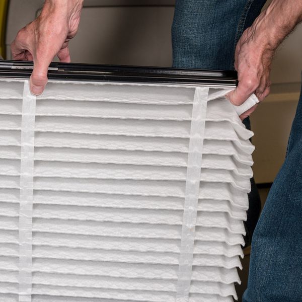 A repair man sliding in a clean filter into an HVAC system.