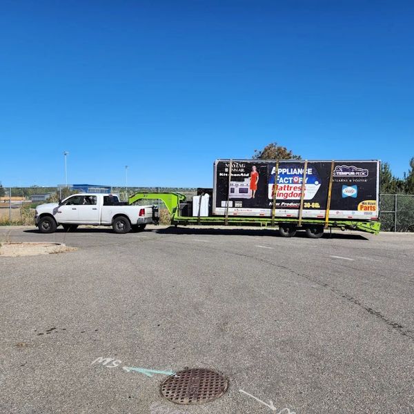 A white pickup truck pulling a flatbed trailer with a large, double-sided mobile billboard or display on it, parked in an asphalt lot under a bright blue sky. A white pickup truck pulling a flatbed trailer with a large, double-sided mobile billboard or display on it, parked in an asphalt lot under a bright blue sky.