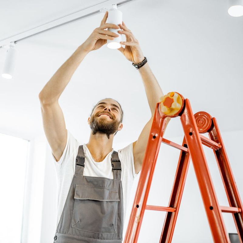 person on ladder installing light fixture in ceiling