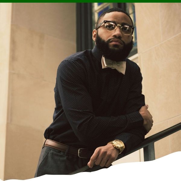 black man in sweater and glasses leaning on railing