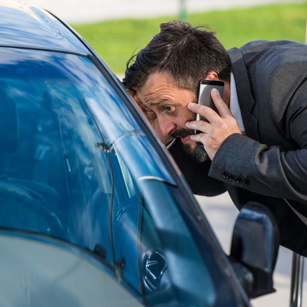 man on the phone peering into car after being locked out