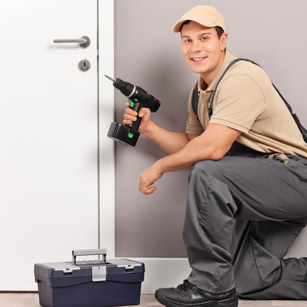 Locksmith holding a drill and kneeling while smiling. 