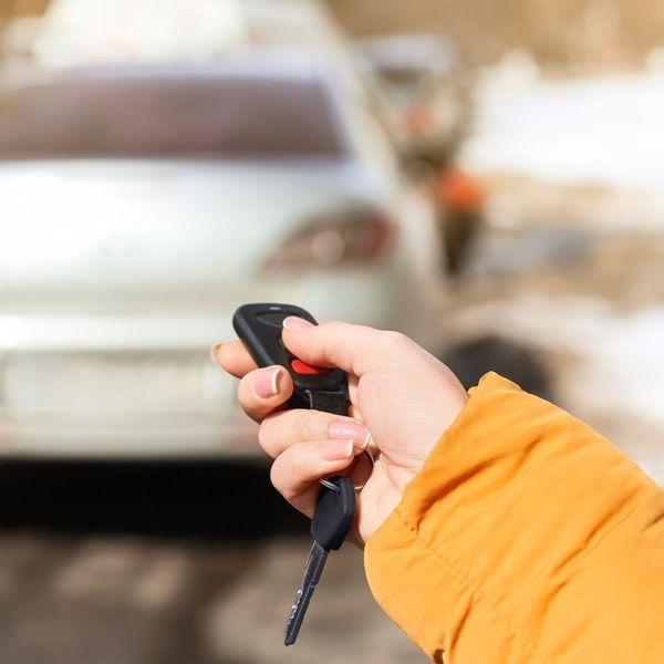 woman in yellow jacket pointing key fob towards her car
