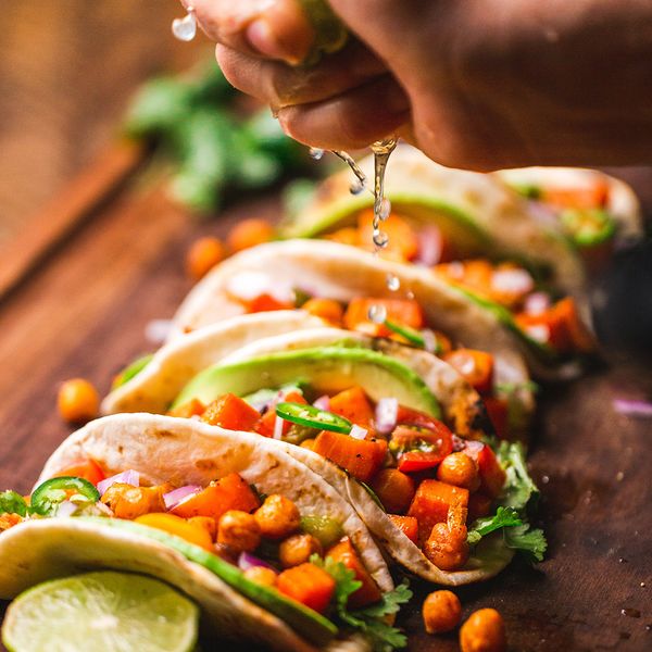 A lime being squeezed over freshly prepared street tacos