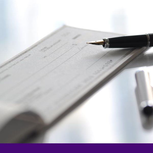 A close-up of a black and silver fountain pen lying across a blank check in an open checkbook. A close-up of a black and silver fountain pen lying across a blank check in an open checkbook.