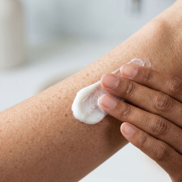 An intimate, close-up view of diverse hands applying a luxurious white skincare cream to freckled skin, highlighting hydration and texture.