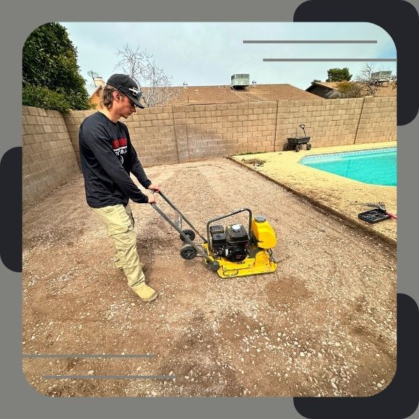 Worker compacting soil near a pool area.