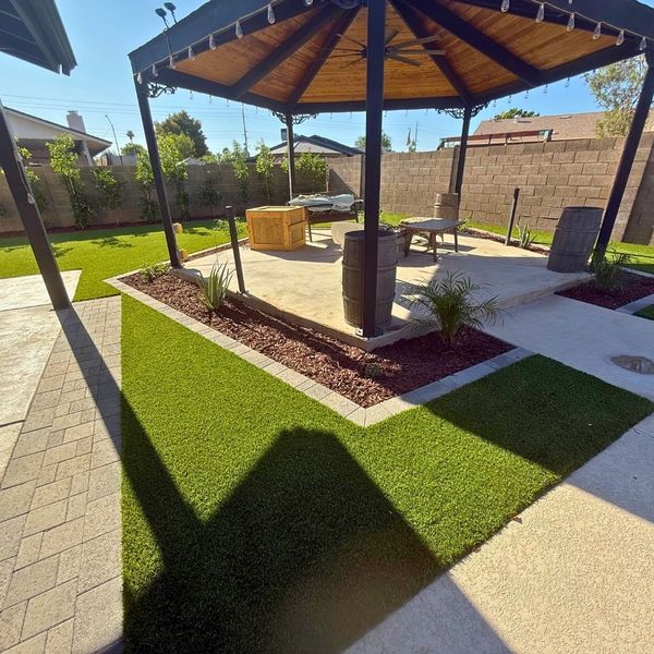 A freestanding wood-ceiling gazebo with integrated lighting and a ceiling fan, surrounded by professionally installed artificial turf and gravel.