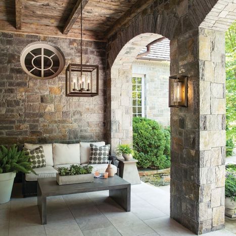 Bronze square cage hanging lantern suspended from a rustic wood ceiling over a covered stone patio seating area.