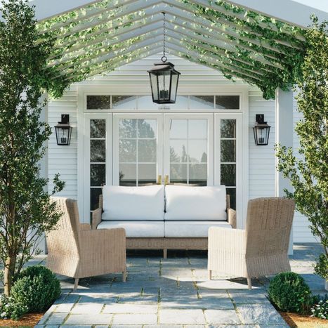 Traditional black outdoor hanging lantern centered under a vine-covered pergola over a patio sofa and armchairs.