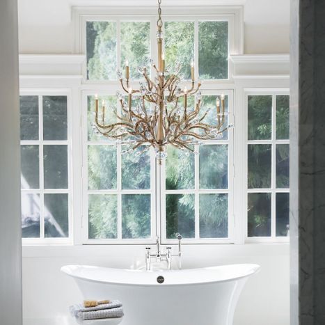 Glamorous brass twig and crystal branch chandelier hanging above a white freestanding soaking tub in a luxury bathroom.