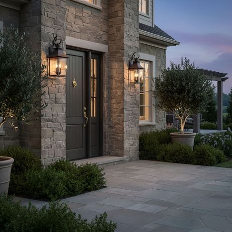 Pair of illuminated black metal outdoor wall lanterns mounted on stone pillars framing a dark front entrance at dusk.