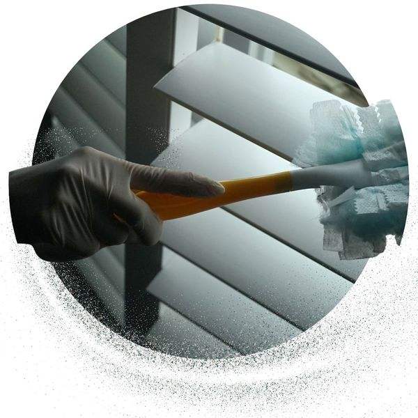 person wearing a glove dusts slats of blinds 
