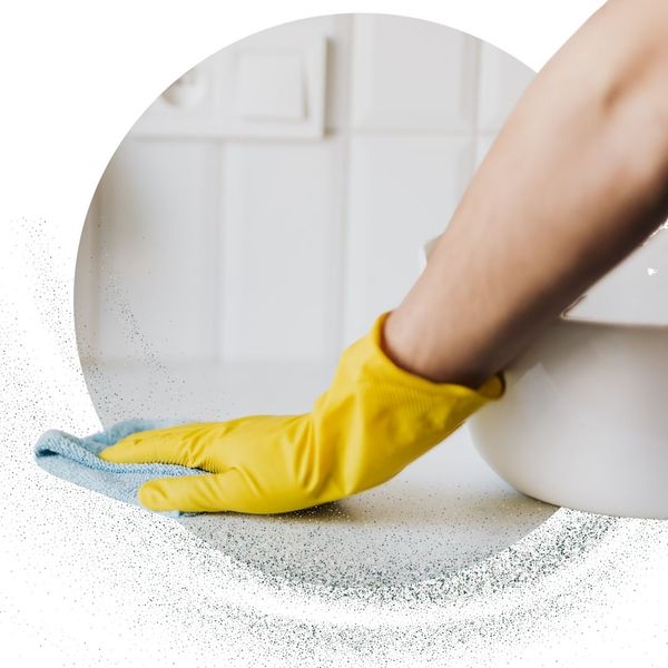 a cleaner wearing a yellow glove wipes a bathroom countertop