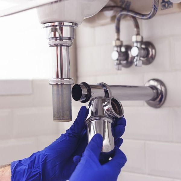 Close-up stock photography of a professional plumber's hands using tools to repair a leaky kitchen faucet in a residential home, illustrating reliable plumbing services.