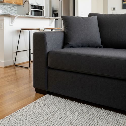 Close-up of a charcoal gray sofa corner resting on a cream-colored textured area rug