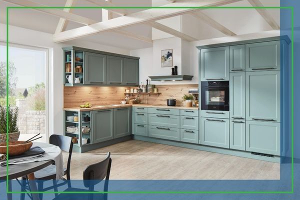 Bright modern kitchen with pale wood ceiling beams, green shaker cabinets, a built-in oven, and a central island, plus a dining table with chairs on the left.