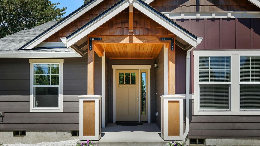 Craftsman style entry door with a light wood finish and small glass lites, beneath a rustic wooden porch.