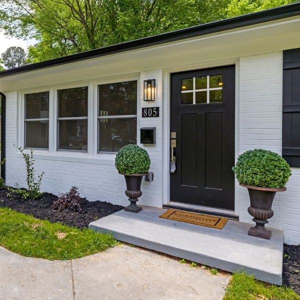 Modern black entry door with multi-pane glass panels, set in a white brick facade with decorative shrubs. Modern black entry door with multi-pane glass panels, set in a white brick facade with decorative shrubs.