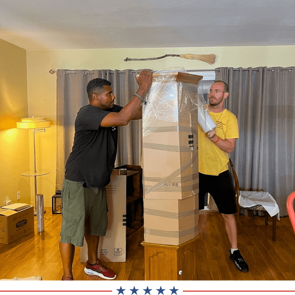 two movers wrapping a large piece of furniture