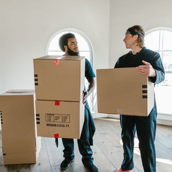 Two movers holding boxes in an empty living room