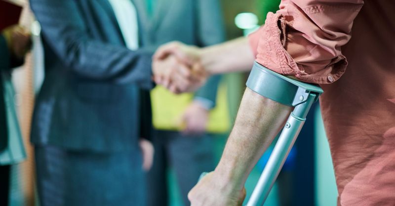 Close up of someone with a walking crutch shaking a lawyer's hand