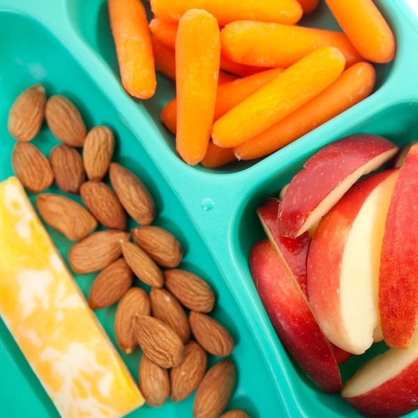 A close-up view of a green segmented lunchbox containing almonds, carrot sticks, and sliced red apples. A close-up view of a green segmented lunchbox containing almonds, carrot sticks, and sliced red apples.
